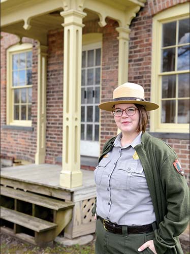 Woman in park ranger uniform in front of brick home
