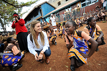 Lauren Lauren kneeling in the red earth of a Kenyan playground and smiling at a Kenyan schoolgirl