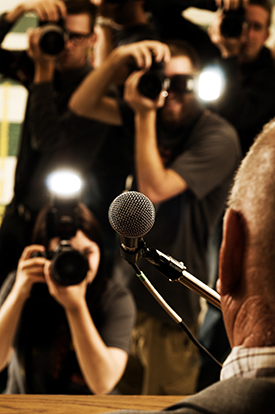 The press taking pictures of a person speaking at a microphone