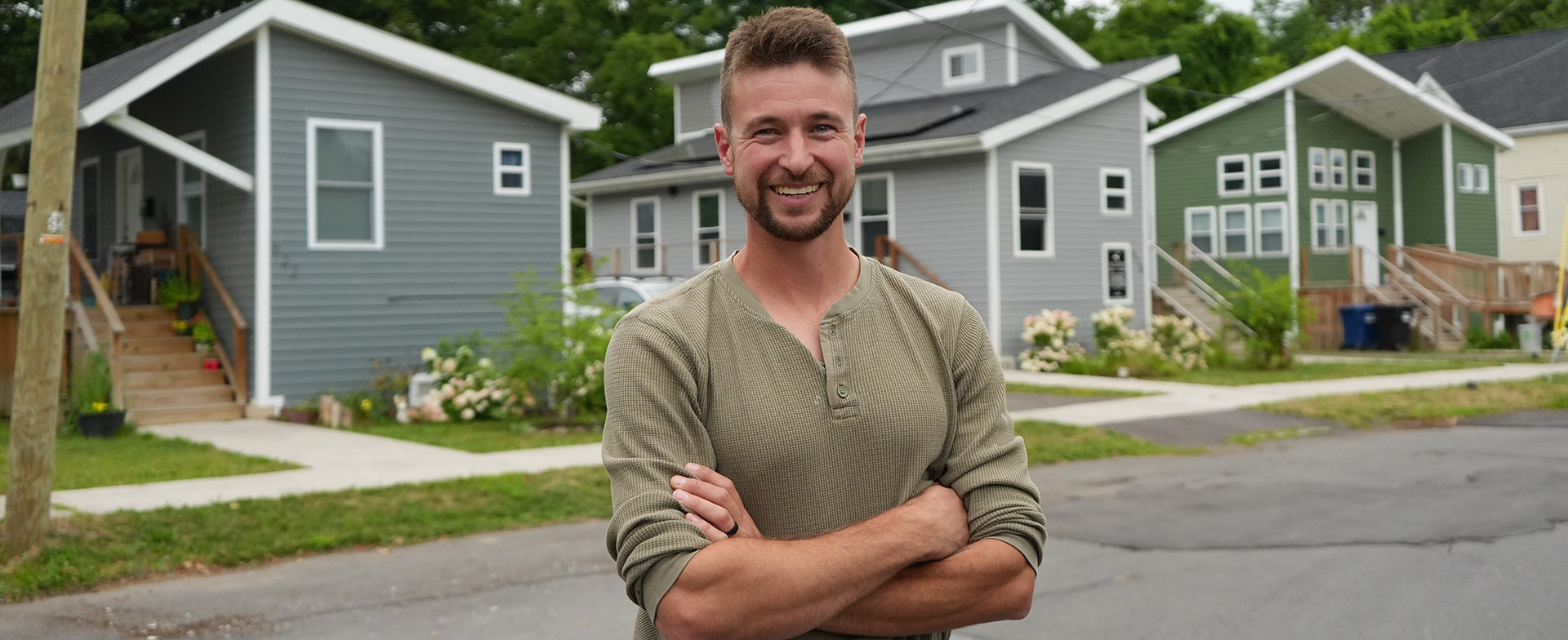 A person stands with arms crossed on a street lined with tiny homes.