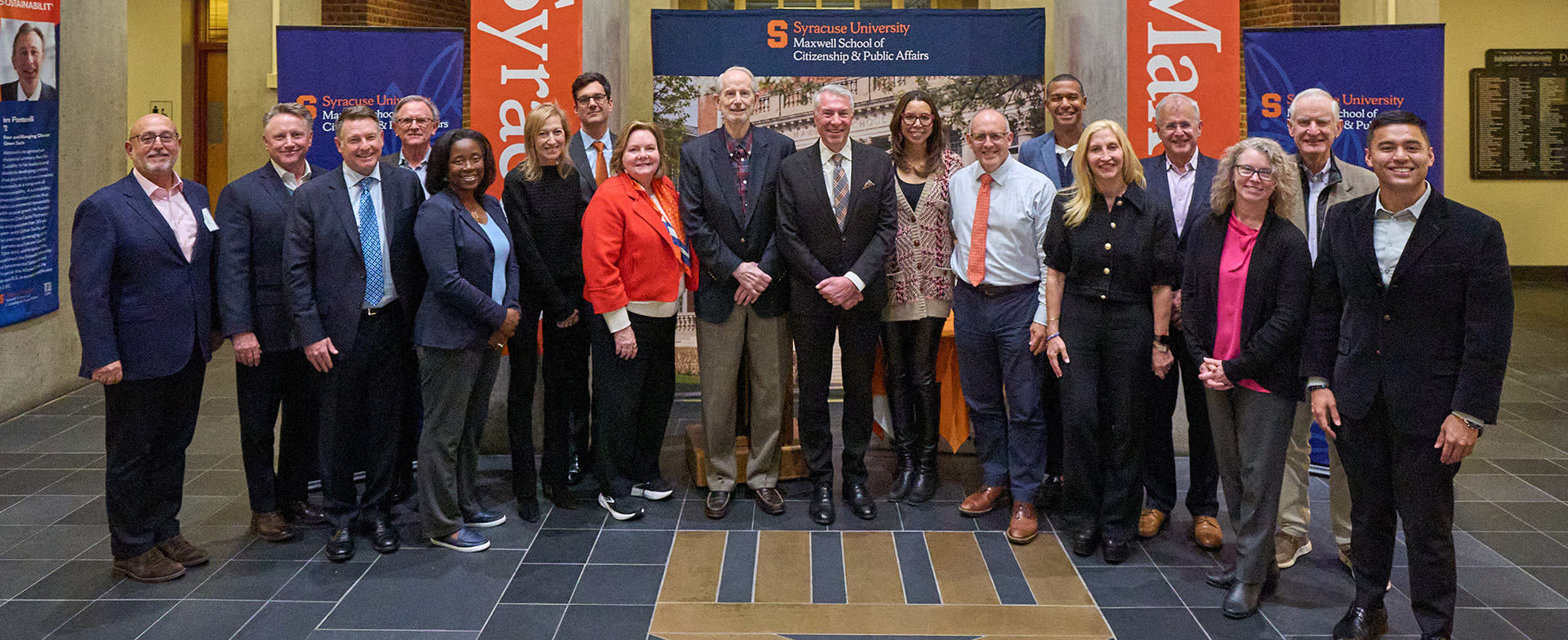 Group of diverse professionals smiling and posing together at Syracuse University's Maxwell School of Citizenship and Public Affairs.