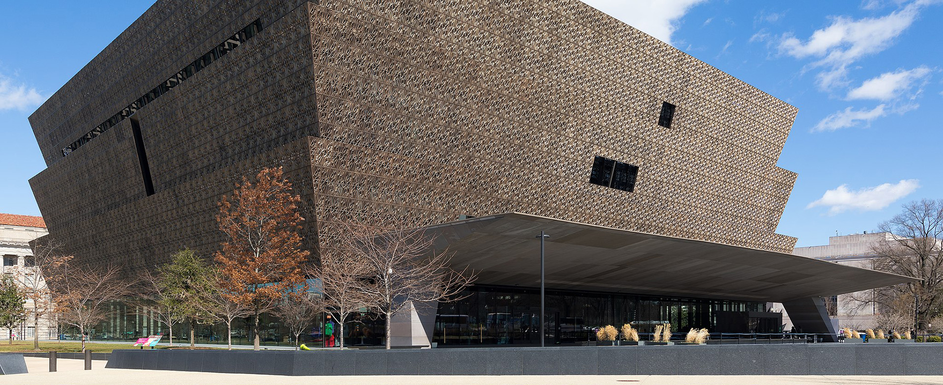Exterior view of the National Museum of African American History and Culture, showing its unique three-tiered, bronze-colored facade and large glass entrance.