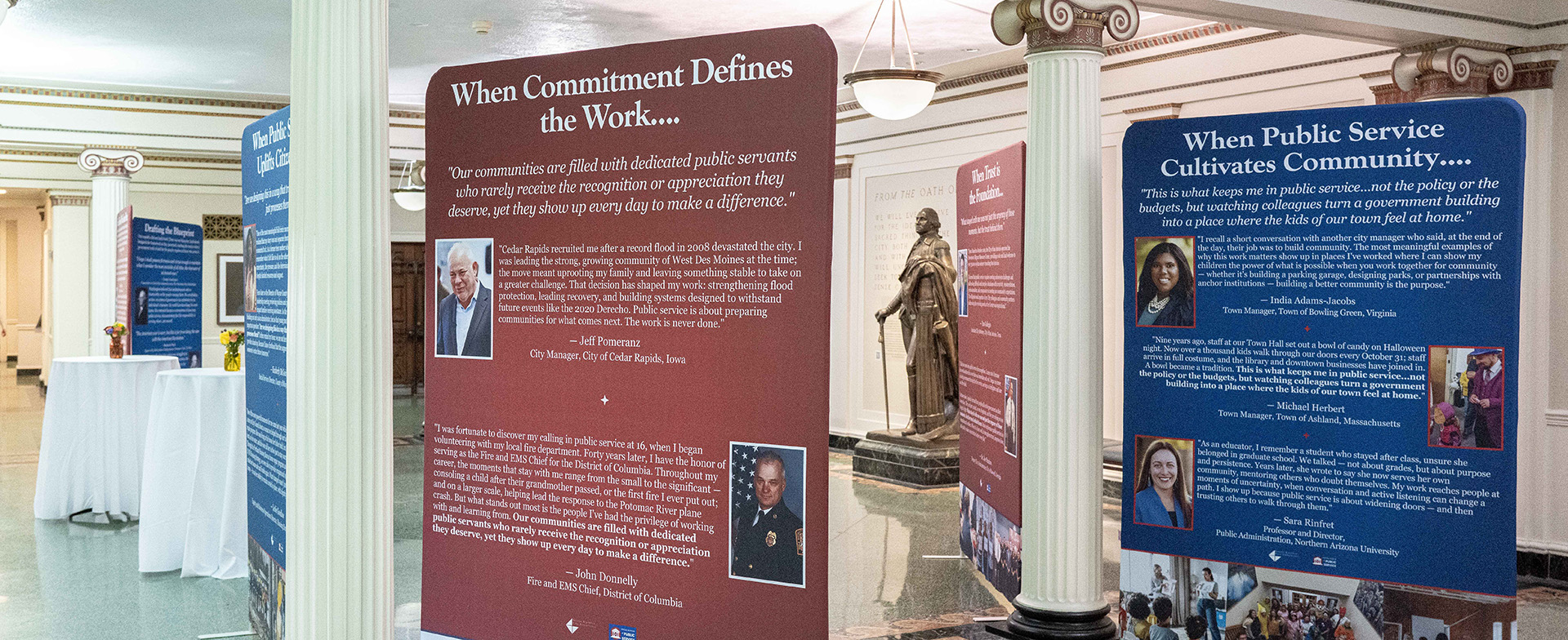 Exhibit banners on public service displayed among columns near a statue.