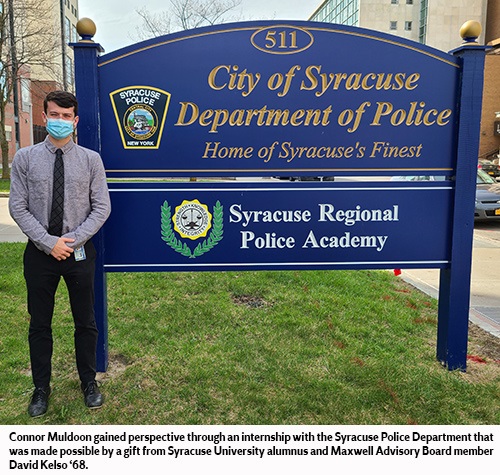 Male student stands next to a blue police department sign outside