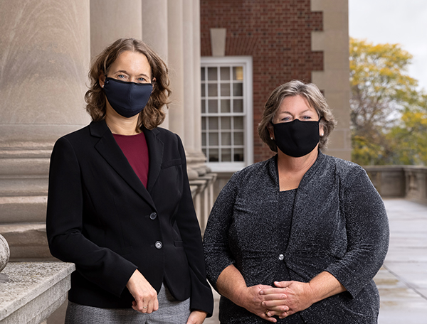 Professors Colleen Heflin and Madonna Harrington Meyer posing with masks on the Maxwell Foyer