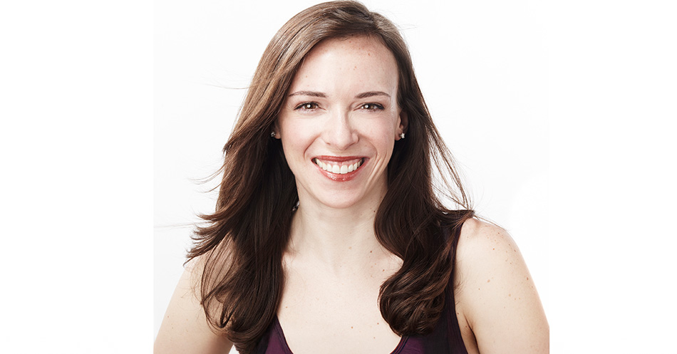 Portrait of a smiling person with long brown hair, wearing a purple top, against a white background.