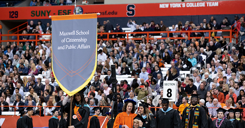 Students walking into commencement with Maxwell sign