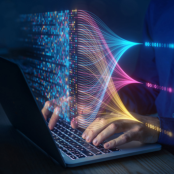 A person types on a laptop keyboard with a colorful digital illustration of flowing data streams and binary code projected above it, representing artificial intelligence or data processing.