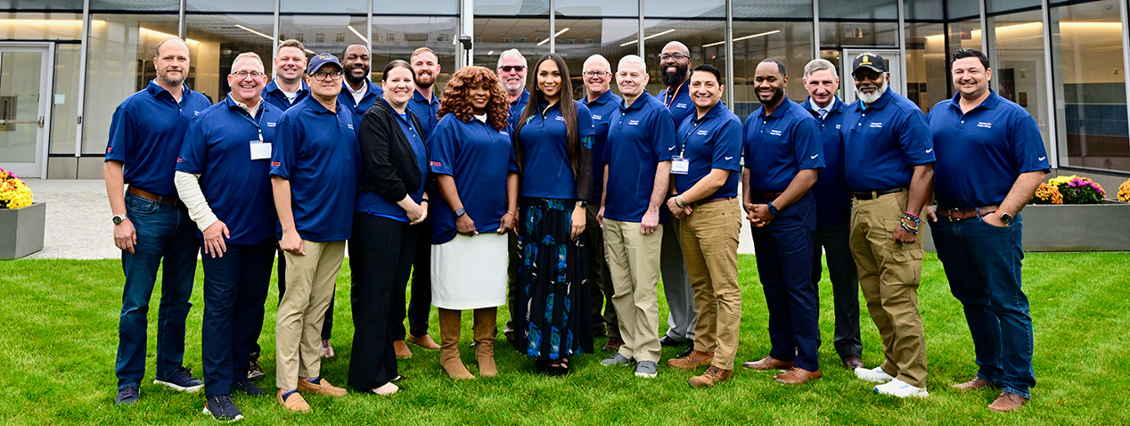 Group of people standing on grass. All are wearing blue polo shirts.