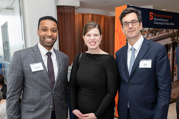 Three attendees pose together at the Maxwell School of Citizenship and Public Affairs Awards of Excellence event, with a Syracuse University Maxwell School banner visible in the background.