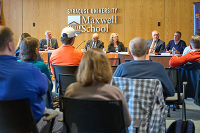 Panel discussion at Syracuse University's Maxwell School, featuring multiple speakers addressing an audience.