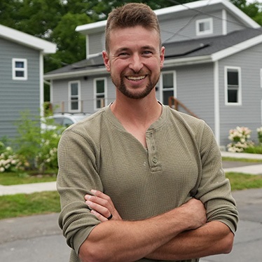 A person stands with arms crossed on a street lined with tiny homes.