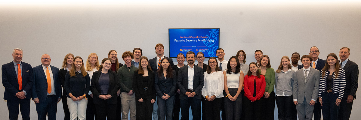 Group of people posing for a photo at the Maxwell School, standing in front of a sign that reads