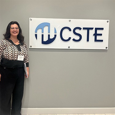 Person standing next to a wall-mounted sign that reads "CSTE."