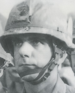 A person in a military helmet with chin strap, serious expression.