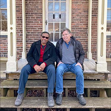 Two men sitting on the porch of an old brick home