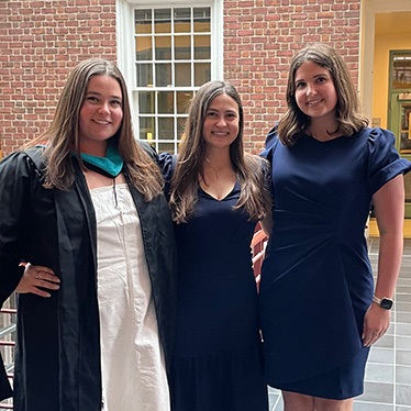 Three graduates in commencement attire pose together in a brick courtyard.