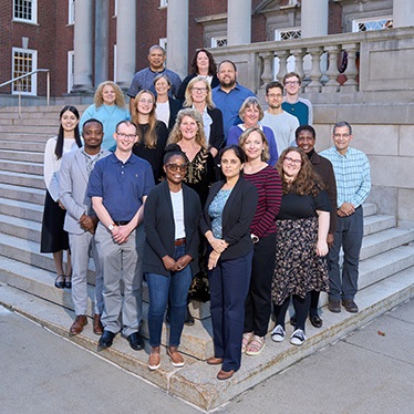 Group of diverse people posing on steps in front of a traditional brick building.