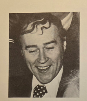 A black and white photo of a person smiling in a suit and polka dot tie.
