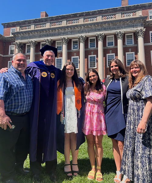 Six people gather outside a columned building to celebrate a graduate.