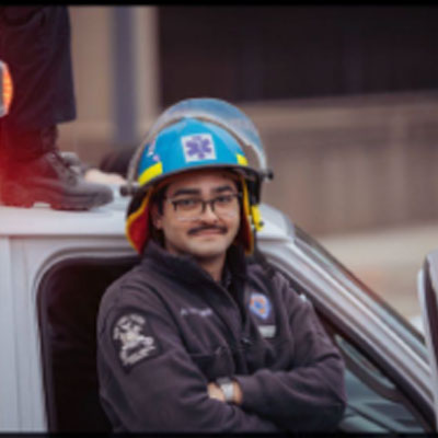 Aric dressed in an EMS outfit leans against an ambulance