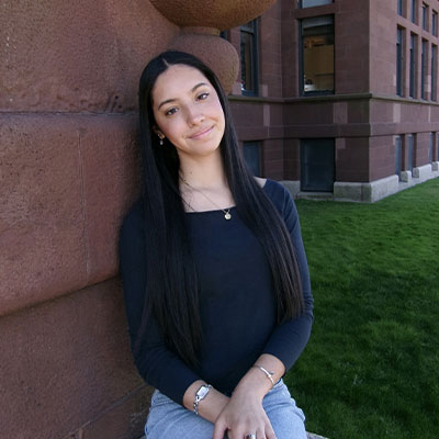 Sophia Lehrer Leans against on of Falk College's buildings.