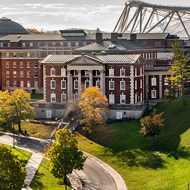 Aerial view of a brick campus building with columns, surrounded by trees and green lawns.