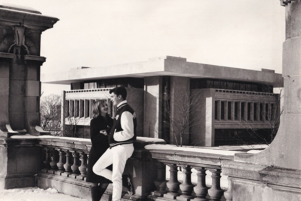 Two people talking on a stone balustrade near a modern building.