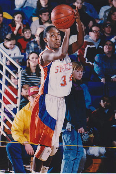 A basketball player wearing a Syracuse jersey, number 34, is taking a free throw during a game as spectators watch in the background.