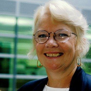 Portrait of a person wearing glasses and smiling in front of a blurred background.
