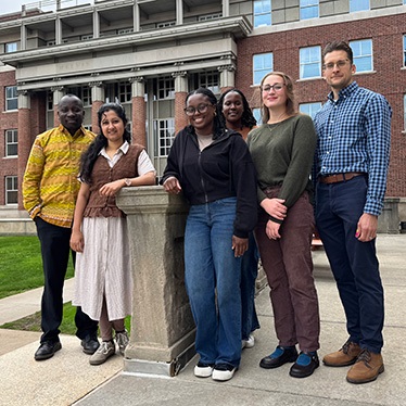 Six public health researchers posing together outside brick campus building.