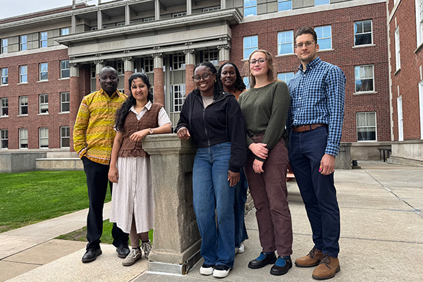 Six public health researchers posing together outside brick campus building.