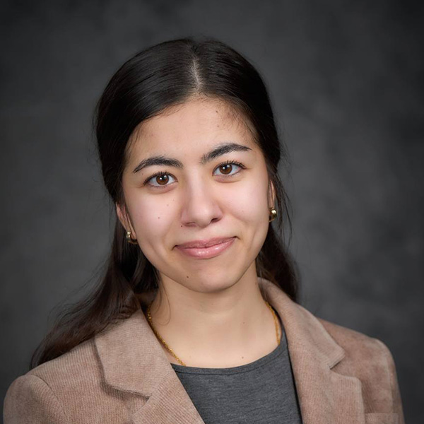 Portrait of a smiling individual with long dark hair, wearing a beige blazer.