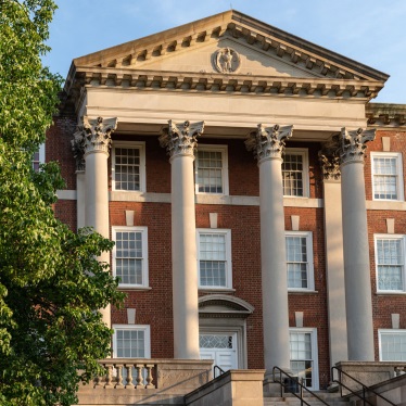 Brick campus building facade with tall white columns and pediment, late spring light.