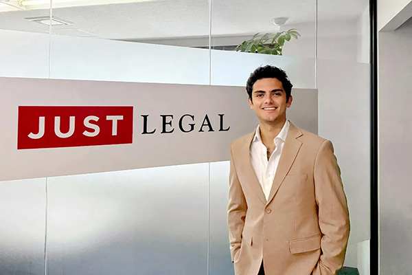 Person in a beige suit standing in an office with a sign that reads