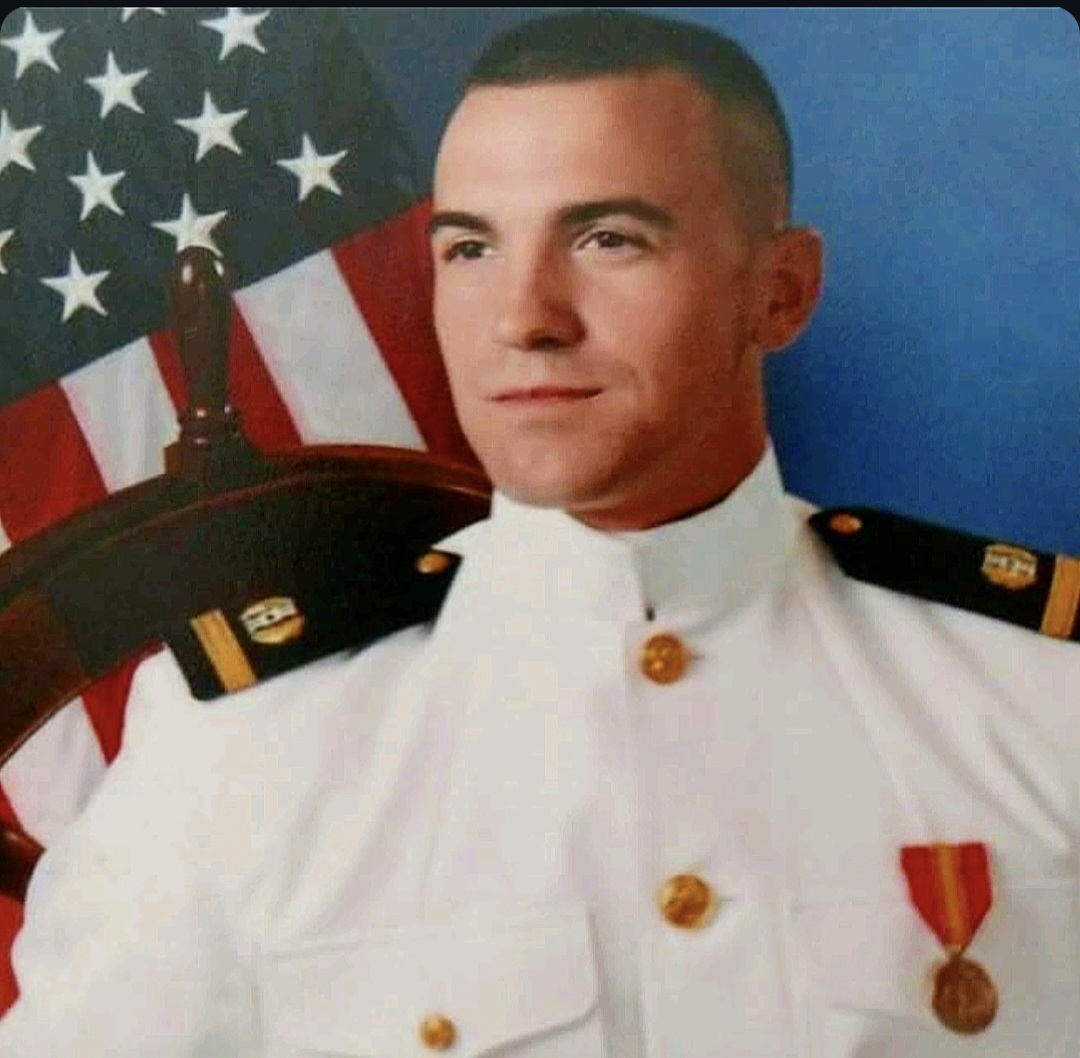 U.S. Marine in dress uniform posing in front of an American flag.