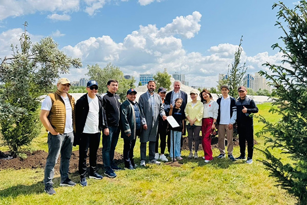 Group of people posing outdoors in a park with trees and a cloudy sky in the background.
