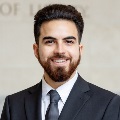 A person with a beard, smiling, wearing a dark suit and tie