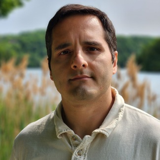 A person wearing a cream polo shirt with a lake and tall reeds in the background.