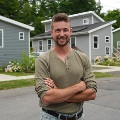 A person stands with arms crossed on a street lined with tiny homes.
