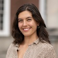 Portrait of a smiling person with shoulder-length brown hair, wearing a beige top.