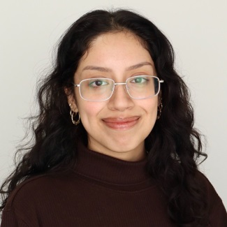 A person curly dark hair, glasses, hoop earrings, brown turtleneck sweater.