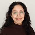 A person curly dark hair, glasses, hoop earrings, brown turtleneck sweater.