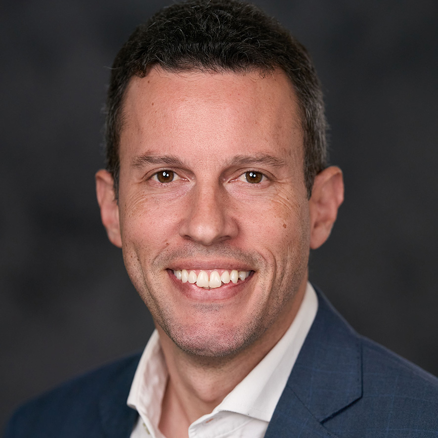 Portrait of a smiling person in a blue suit against a dark gray background.