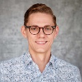 Person with short blond hair wearing glasses and a blue patterned shirt.