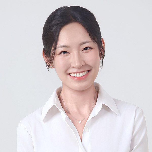 A person smiling in white collared shirt with a delicate necklace.