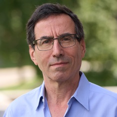 Close-up portrait of an individual wearing a blue shirt against a blurred green background.