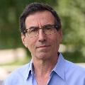 Close-up portrait of an individual wearing a blue shirt against a blurred green background.