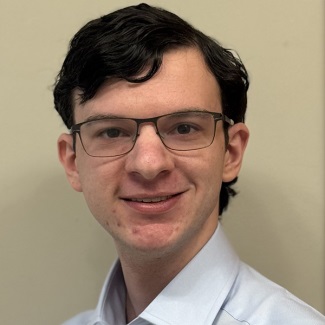 A person with dark hair and glasses weaing a collared shirt.