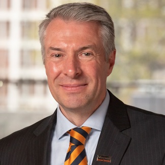 Portrait of a person wearing a suit and a striped tie, smiling in front of a blurred background.